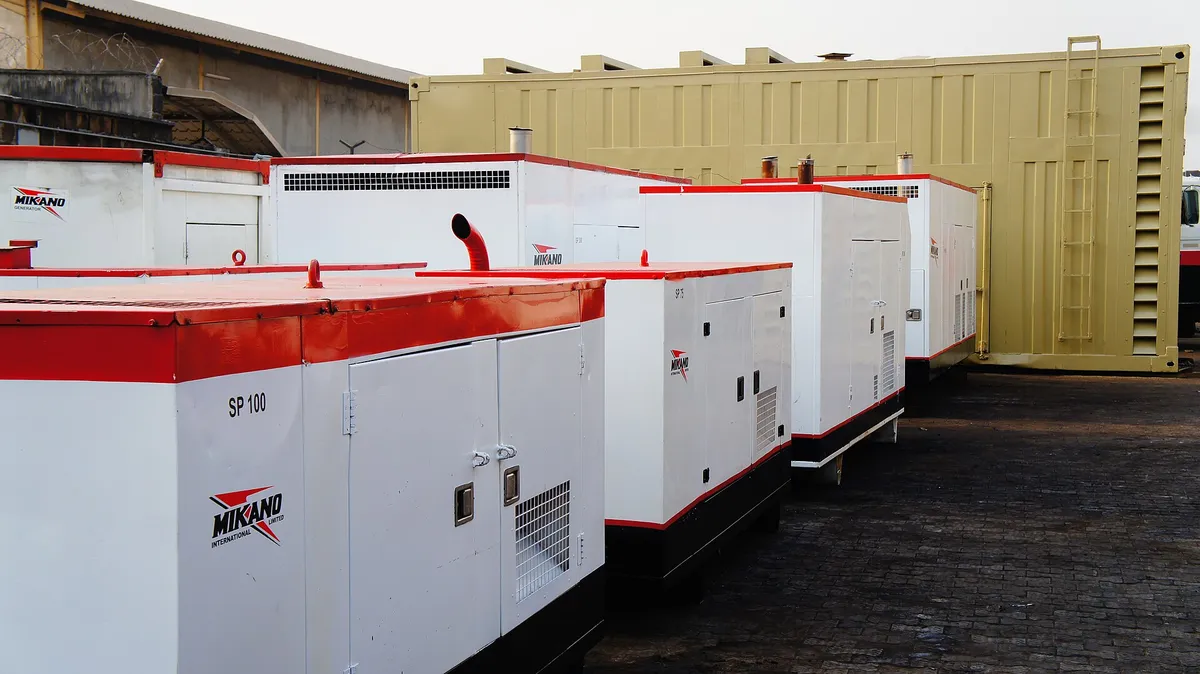 Beberapa genset berkanopi putih berpinggang merah dengan ukuran berbeda berderet di halaman beraspal